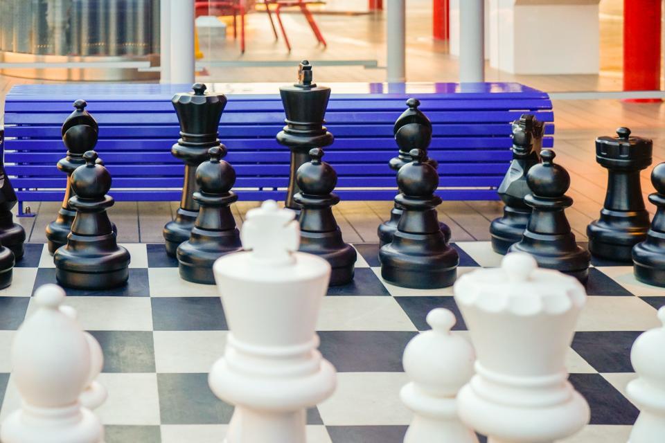 A black and white jumbo chess set in front of a blue bench on a cruise ship deck