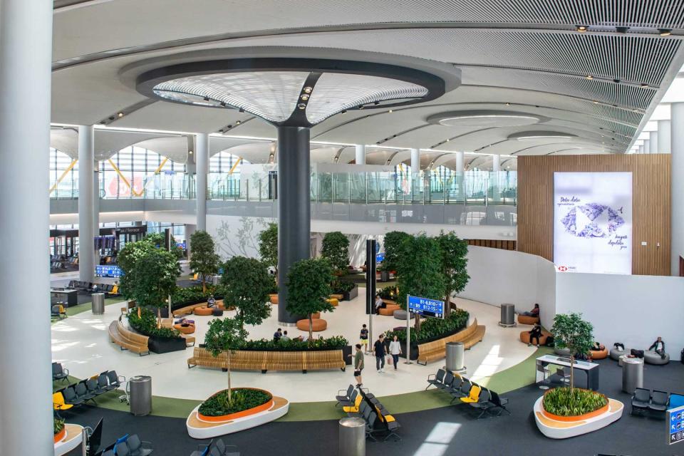 Large open waiting space in Istanbul's modern international airport, with passengers walking throughout the area prior to boarding their flights from nearby gates - Istanbul, Turkey