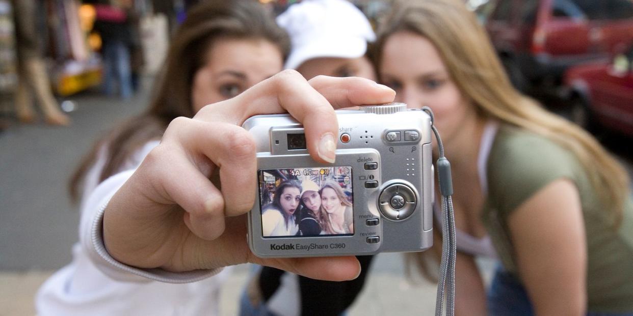 three girls using a kodak digital camera to take a photo together