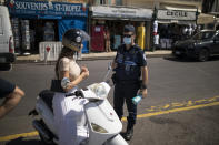 A police officer informs a woman about the mandatory face mask requirement in Saint-Tropez, southern France, Saturday Aug 8, 2020. The glamorous French Riviera resort of Saint-Tropez is requiring face masks outdoors starting Saturday, threatening to sober the mood in a place renowned for high-end, free-wheeling summer beach parties. (AP Photo/Daniel Cole)