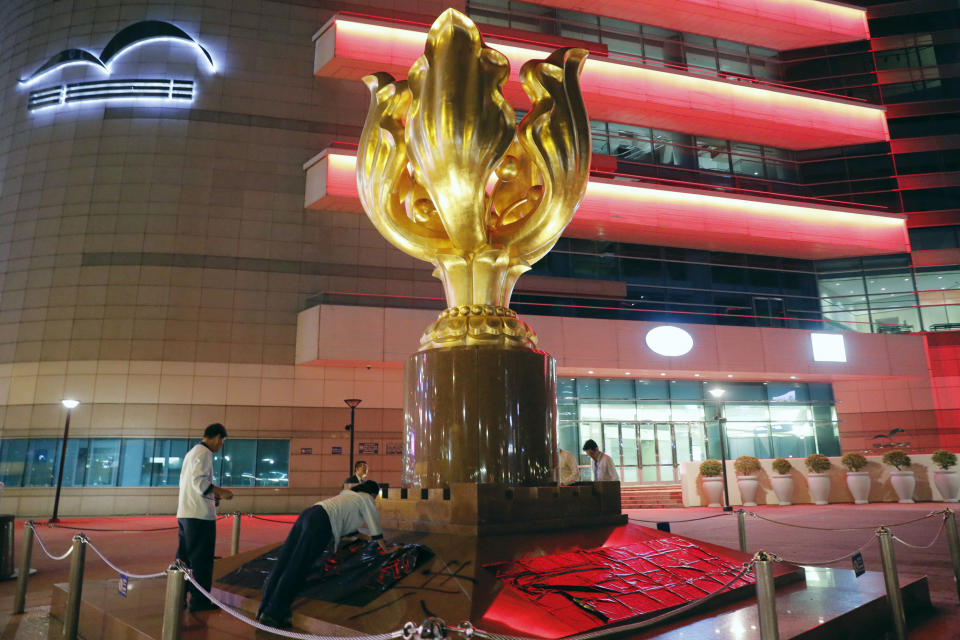 Workers cover graffiti sprayed on the base of a giant flower statue bequeathed by Beijing in 1997 in Golden Bauhinia Square in Hong Kong on Sunday, Aug. 4, 2019. Demonstrators in Hong Kong moved en masse to a luxury shopping district Sunday evening after riot police used tear gas to clear out an area they were previously occupying, as the 2-month-old protest movement showed no signs of easing. (AP Photo/Kin Cheung)