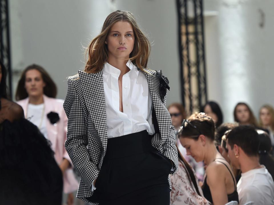 Model walks runway wearing classic blazer and white button down shirt