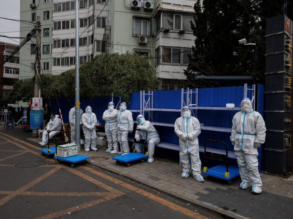 line of masked workers in white biohazard suits in front of blue barrier blocking off housing compound