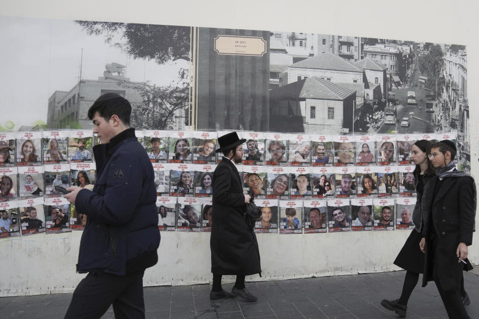 People pass by a wall with photos of about 240 hostages who were abducted during the Oct. 7, Hamas attack on Israel. in Jerusalem on Tuesday, Nov. 28, 2023. (AP Photo/Mahmoud Illean)