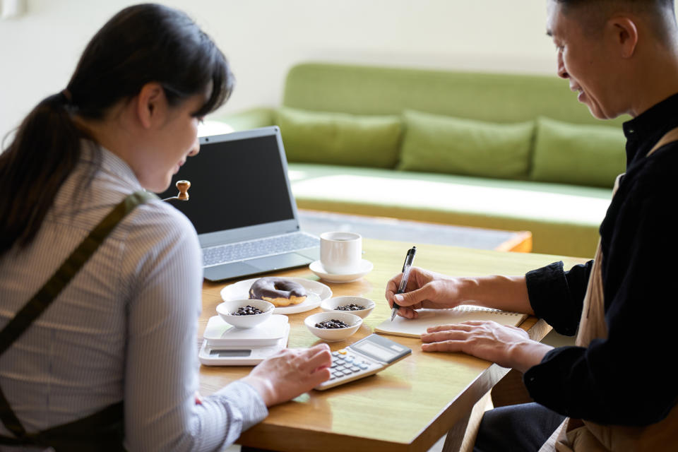 Two people sitting at a table with coffee and snacks and working with a laptop