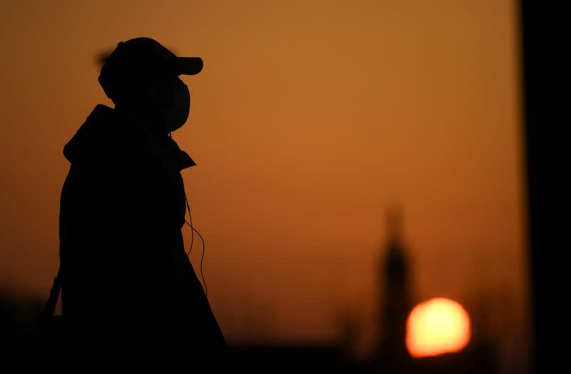 A person wearing a face mask is seen at the sunset as the spread of coronavirus disease (COVID-19) continues, in Milan