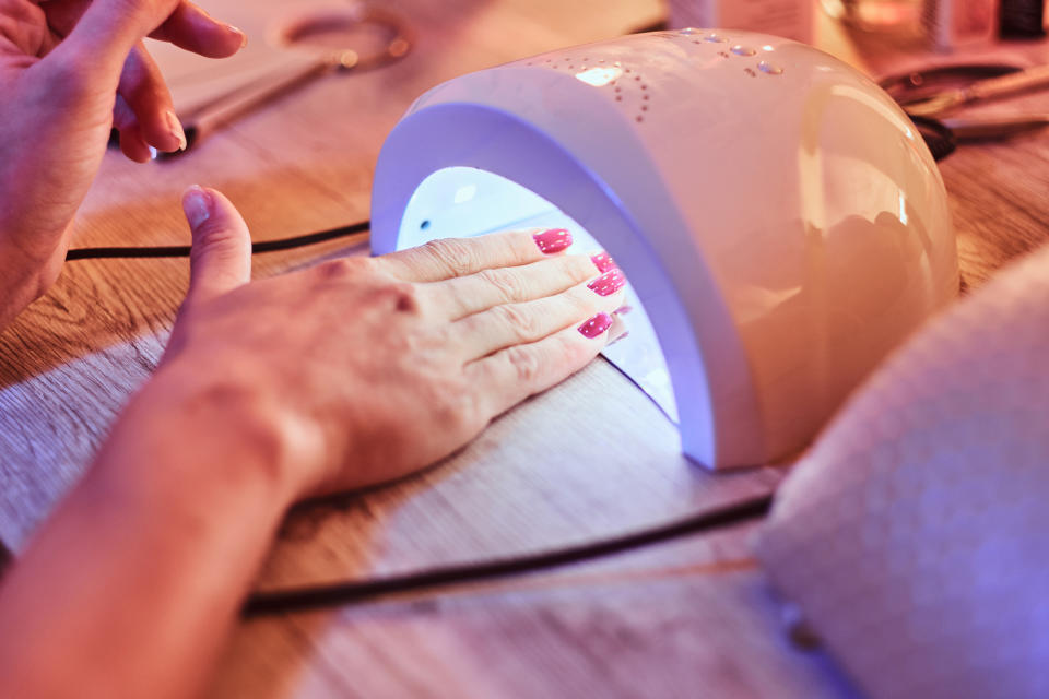 Client with red varnish at manicure salon dryes gel polished nails in UV light. Closeup shoot.