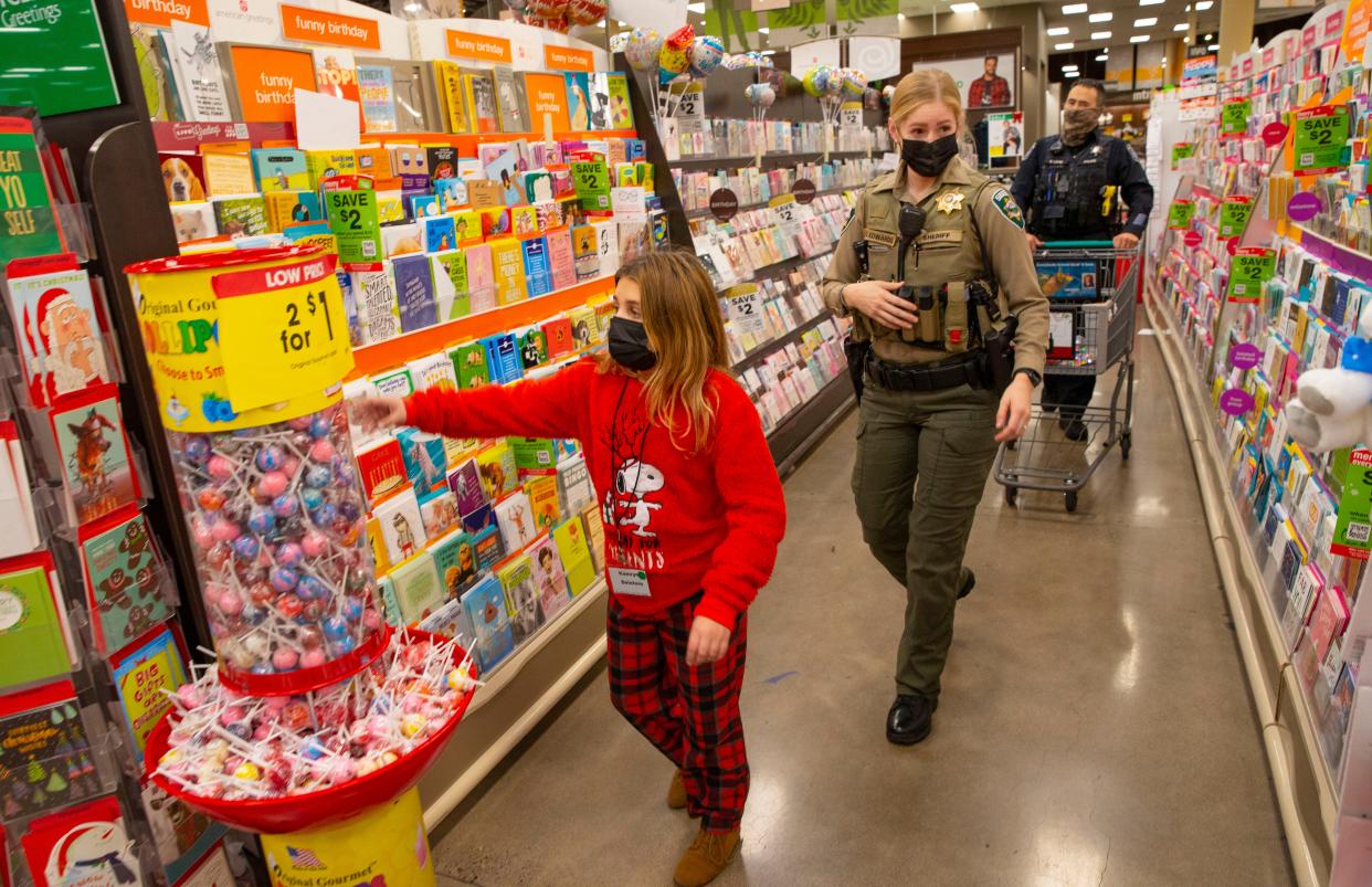 Lane County Sheriff Deputy Emma Edwards, center, and Eugene Police Detective Rick Lowe do their best to keep up with 9-year-old Kamryn Delatore, left, during the annual Shop with a Cop event at Fred Meyer in Eugene on Saturday.