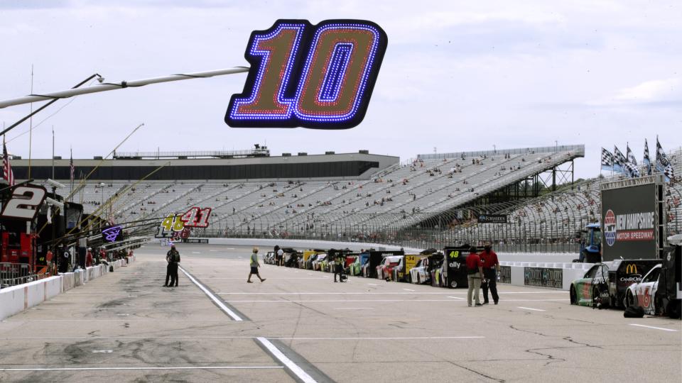 Fans sit socially distanced due to the coronavirus pandemic in the grandstand, rear, as a sign hangs over the pit location for driver Aric Almirola (10) before a NASCAR Cup Series auto race, Sunday, Aug. 2, 2020, at the New Hampshire Motor Speedway in Loudon, N.H. (AP Photo/Charles Krupa)