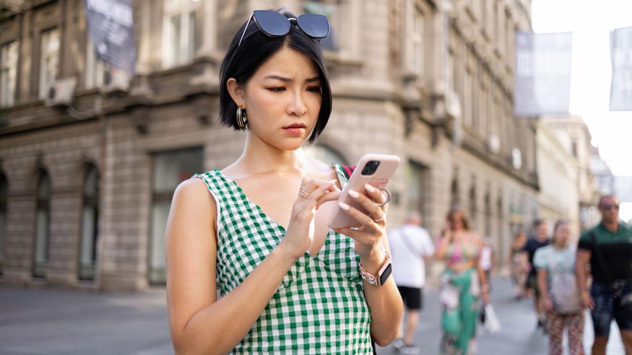 woman out on city sidewalk looking concerned at her smartphone