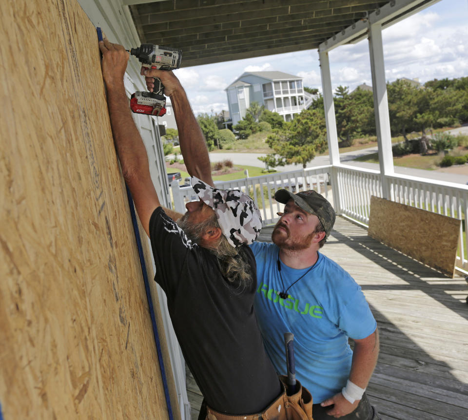 FILE - In this Wednesday, Sept. 12, 2018 file photo, Joe Gore, left, and Joshua Adcock prepare for Hurricane Florence as they board up windows on a home in Emerald Isle N.C. Before and after a hurricane, Ace is the place. And Home Depot, Lowe’s, and many other hardware and building supply outlets. Not surprisingly, these companies plan for storms such as Hurricane Florence all year. (AP Photo/Tom Copeland, File)