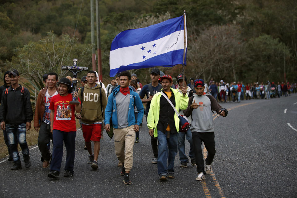 Honduran migrants walk north along a road in hopes of reaching the distant United States, one carrying a Honduran flag, as they leave Esquipulas, Guatemala, just after sunrise Friday, Jan. 17, 2020. The group departed San Pedro Sula on Jan. 15. (AP Photo/Moises Castillo)