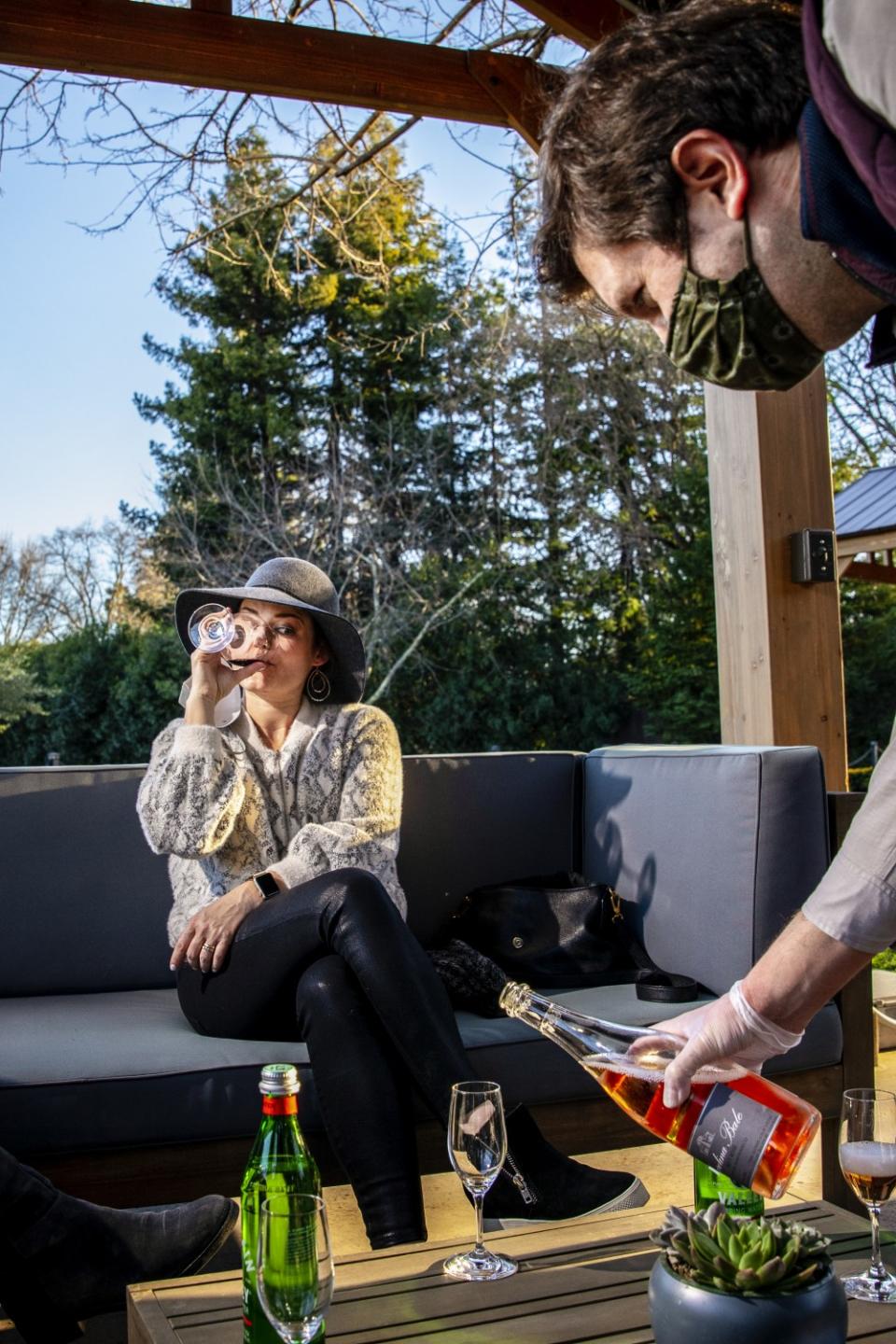 A woman drinks wine as her mask hangs from her ear.