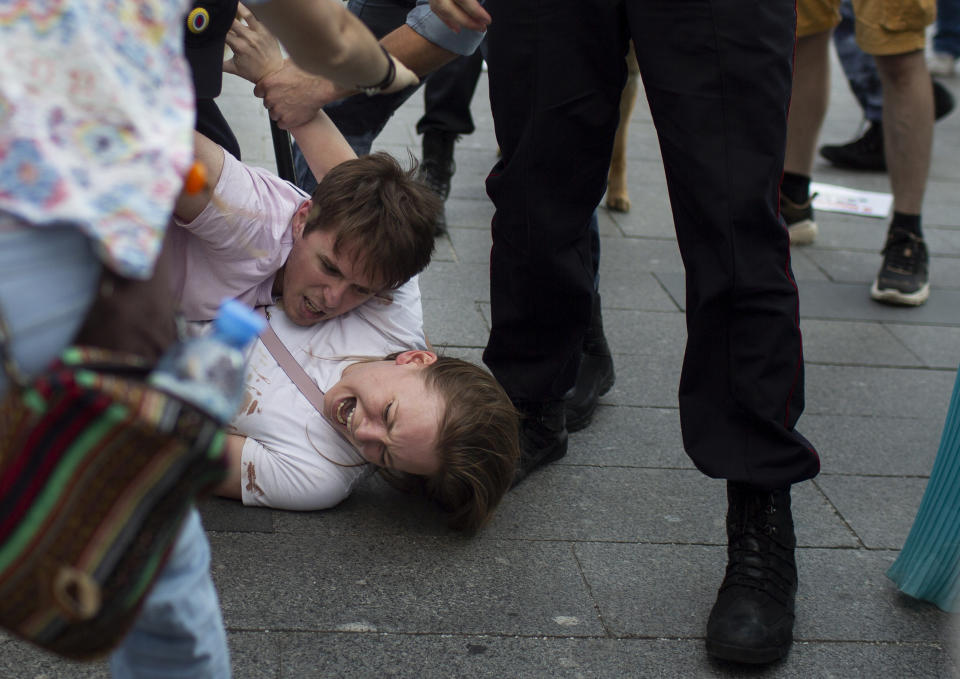 In this photo taken on Saturday, July 27, 2019, Inga Kudracheva screaming as her boyfriend Boris Kantorovich lies atop her while police officers try to detain him during an unsanctioned protest in Moscow. Images of the young couple have been spread on social media. They say the crackdown by police has left them shaken but with their resolve strengthened. (AP Photo/Denis Sinyakov)