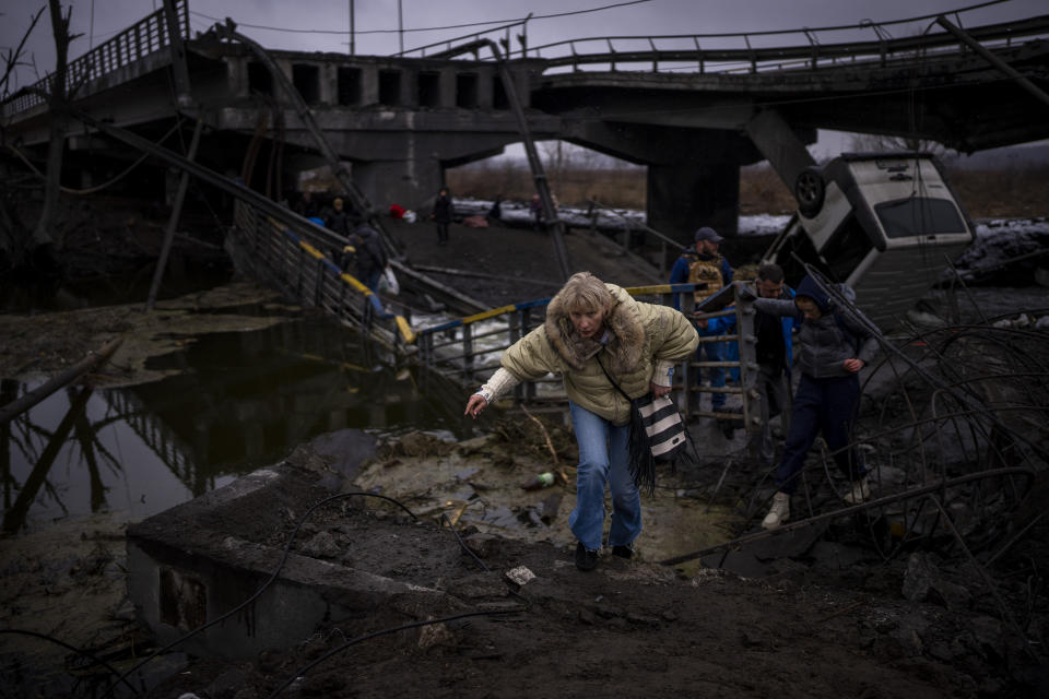 FILE - A woman runs as she flees with her family across a destroyed bridge in the outskirts of Kyiv, Ukraine, Wednesday, March 2. 2022. As milestones go, the first anniversary of Russia's invasion of Ukraine is both grim and vexing. It marks a full year of killing, destruction, loss and pain felt even beyond the borders of Russia and Ukraine. (AP Photo/Emilio Morenatti, File)