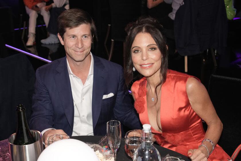 Paul Bernon and Bethenny Frankel in formalwear smile while seated at a dining table