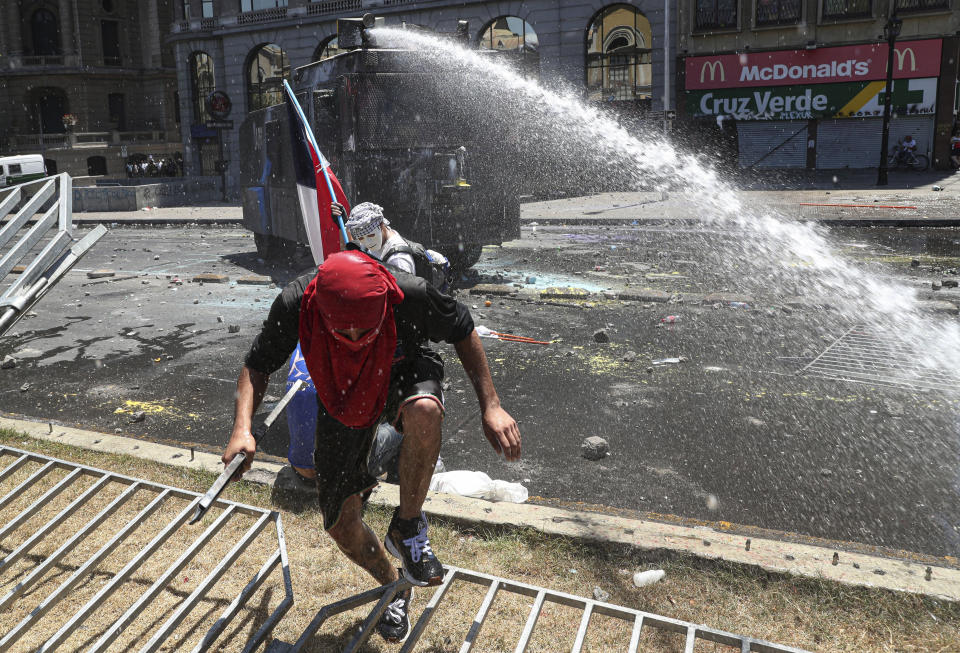 Anti-government demonstrator runs from a police water cannon near La Moneda presidential palace in Santiago, Chile, Tuesday, Nov. 12, 2019. Chile is entering its 26th day of protest against social inequality with huge demonstrations across the country and a national strike. (AP Photo/Esteban Felix)