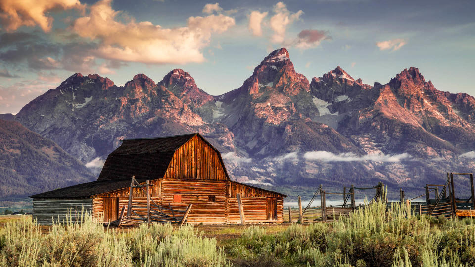 Early morning magenta light illuminates clouds and the Moulton Barn on Mormon Row at the foot of the Grand Tetons near Jackson, Wyoming, USA.