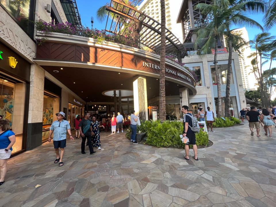 The exterior of a large shopping area with many people walking around.