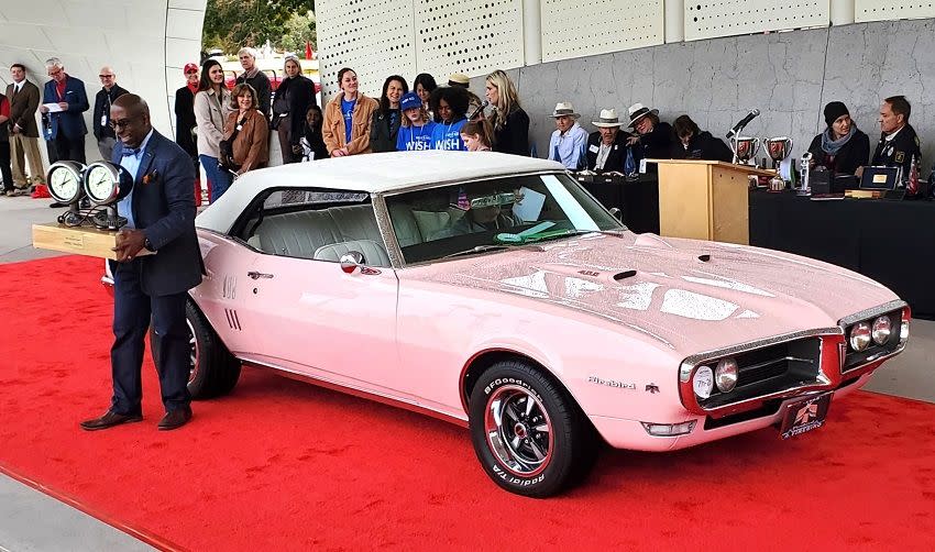 a person standing next to a pink car with people around it