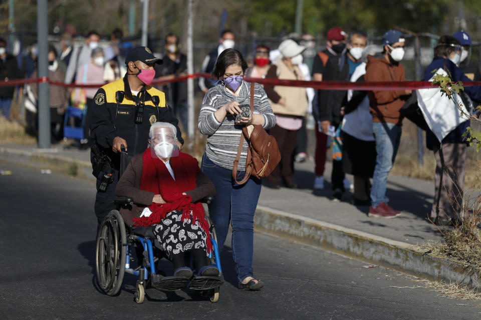 A police officer pushes an elderly woman in a wheelchair to the front of the line as residents of the Iztacalco borough over age 60 wait to get shots of the Sputnik V vaccine for COVID-19 at a vaccination center set up at the Advanced School for Physical Education in Mexico City, Wednesday, Feb. 24, 2021. (AP Photo/Rebecca Blackwell)