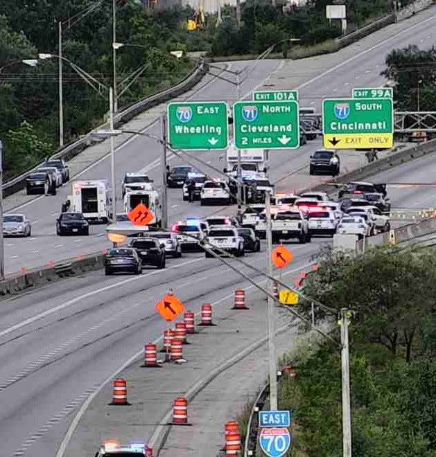 Police vehicles on Interstate 70 east near Mound Street in Columbus surround a stolen black Porsche Cayenne SUV, just beneath the I-71 South sign with doors open, as officers responded Thursday afternoon to a Columbus police officer shot by robbery suspects.