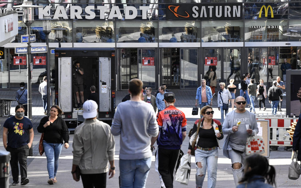 FILE - In this April 20, 2020 file photo, people walk to a shopping center as many smaller stores are allowed to open in Essen, Germany. Europe's biggest economy, starts reopening some of its stores and factories after weeks of lockdown due to the new coronavirus outbreak. (AP Photo/Martin Meissner, File)