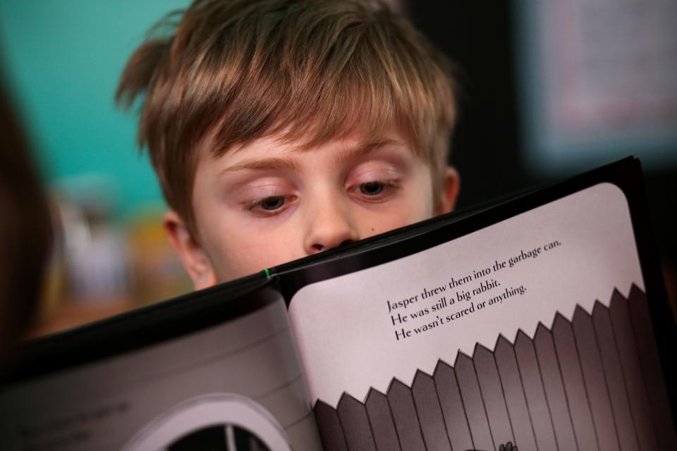 Tommy Minelli, 6, peers over the edge of a book during a video conference call, Thursday, April 2, 2020, in Cincinnati's Northside neighborhood. About a dozen of his mother's colleagues get together and rotate teaching their kids a lesson from a range of subjects.