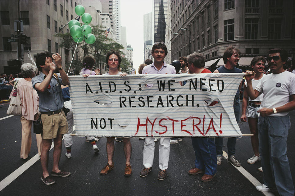 Protesters marching with a banner that says "AIDS we need research not hysteria"