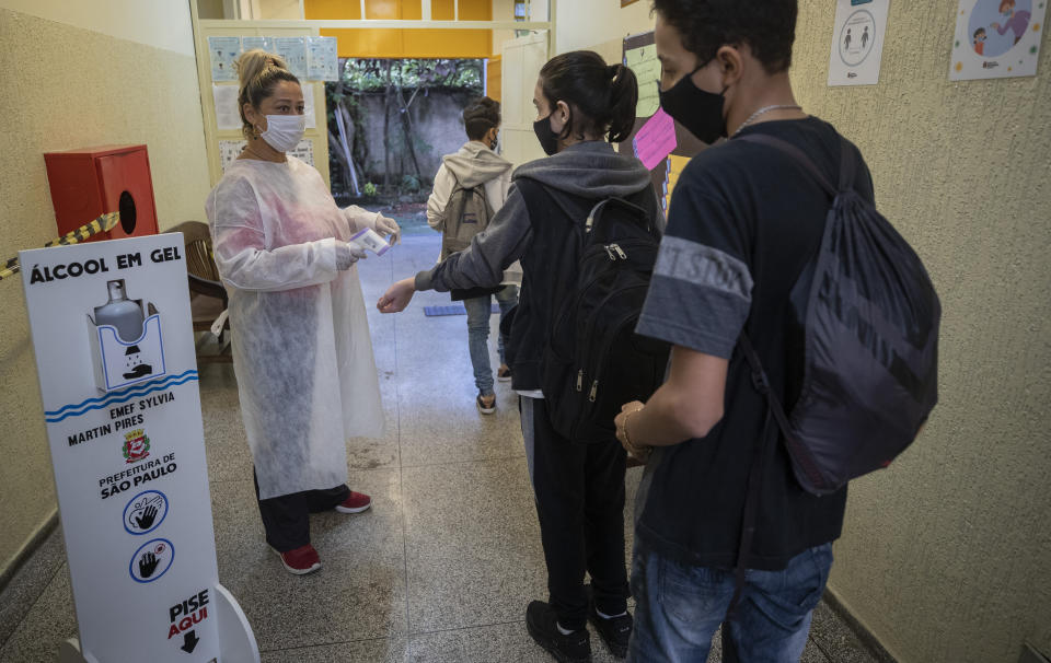 Marilene de Oliveira Paixao toma la temperatura de estudiantes que ingresan a la escuela EMEF Sylvia Martin Pires en Sao Paulo, Brasil, el lunes 8 de marzo de 2021. (AP Foto/Andre Penner)