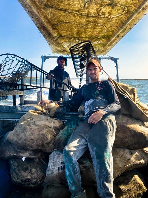 Jacob Hulse sits on bags of oysters as his brother Jason steers the boat toward the dock. The one bright spot in Jacob's life since Hurricane Ida has been the oyster harvest.