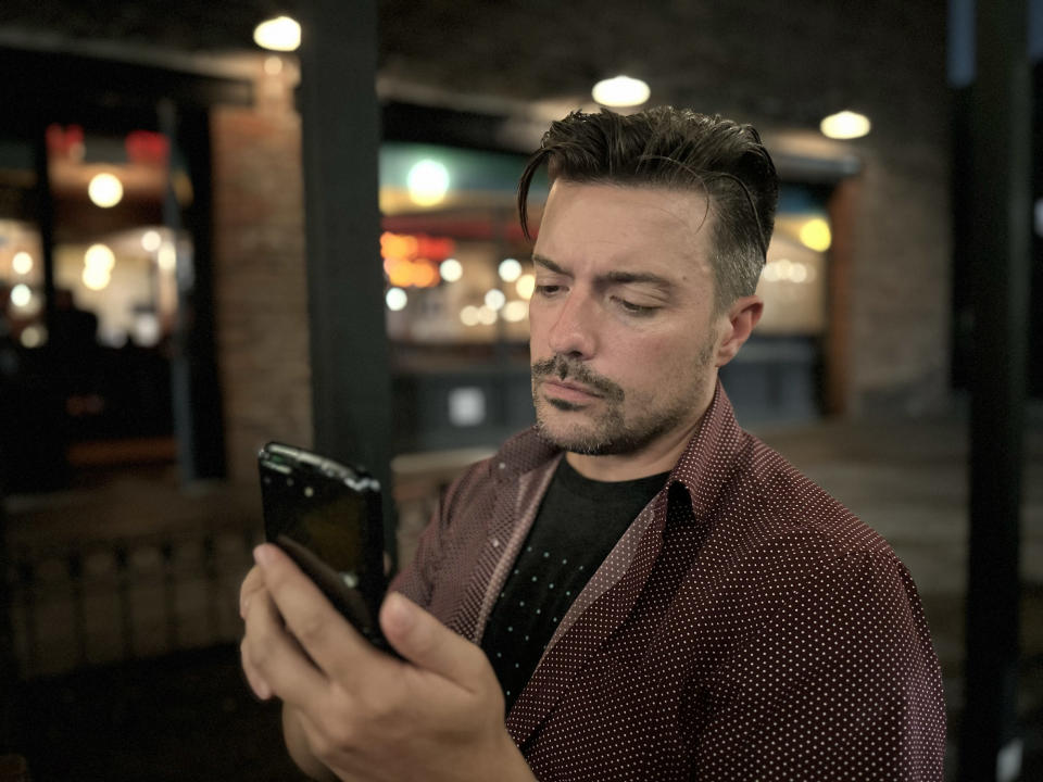 <p>A photo from the iPhone 14's main rear featuring a man looking intently at a foldable Moto Razr phone, with the background around him blurred out.</p>
