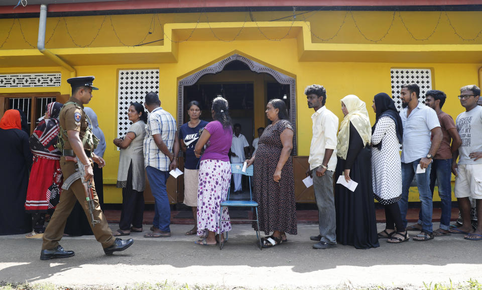 Sri Lankans queue to cast their votes as a police officer stands guard at a polling station during the presidential election in Colombo, Sri Lanka, Saturday, Nov. 16, 2019. Polls opened in Sri Lanka’s presidential election Saturday after weeks of campaigning that largely focused on national security and religious extremism in the backdrop of the deadly Islamic State-inspired suicide bomb attacks on Easter Sunday. (AP Photo/Eranga Jayawardena)