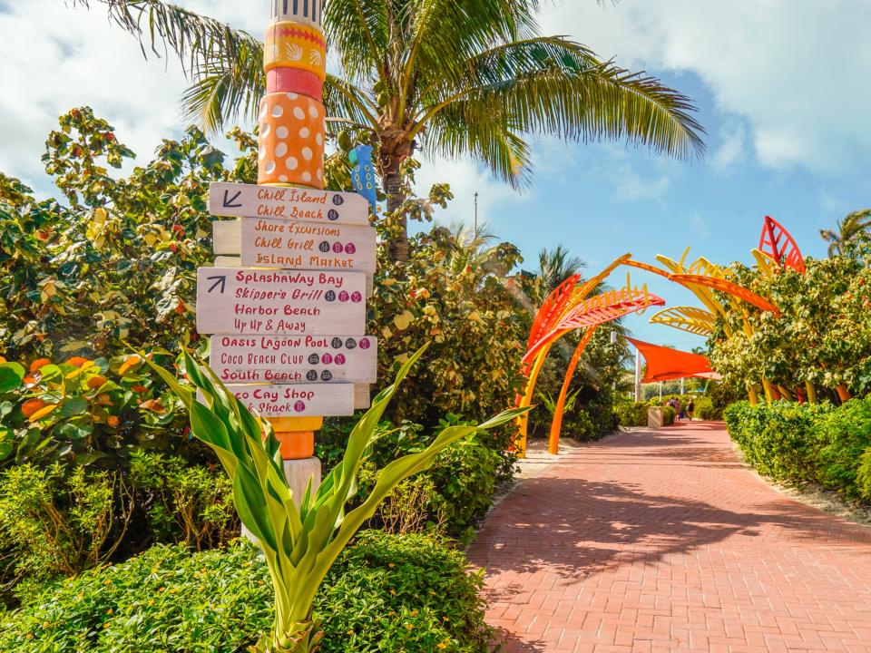 A red path with a sign on the left directing guests at CocoCay on a partly-cloudy day