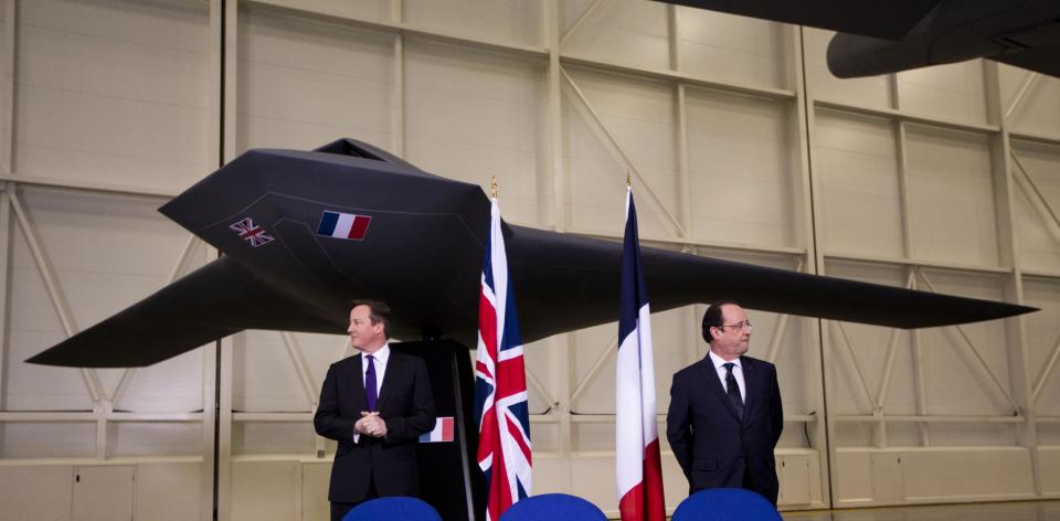 British Prime Minister David Cameron, left, and French President Francois Hollande stand backdropped by a model of a concept design for a future unmanned combat air vehicle as they wait for memorandums of understandings and an agreement to be signed before the start of their press conference at their one-day summit at the RAF Brize Norton air base in Brize Norton, England, Friday, Jan. 31, 2014. The one-day summit covered military cooperation, including talks over armed drones, anti-ship missiles, and underwater mine detectors, as well as a joint Franco-British force of 10,000 soldiers due to be formed in the next few years. (AP Photo/Matt Dunham)