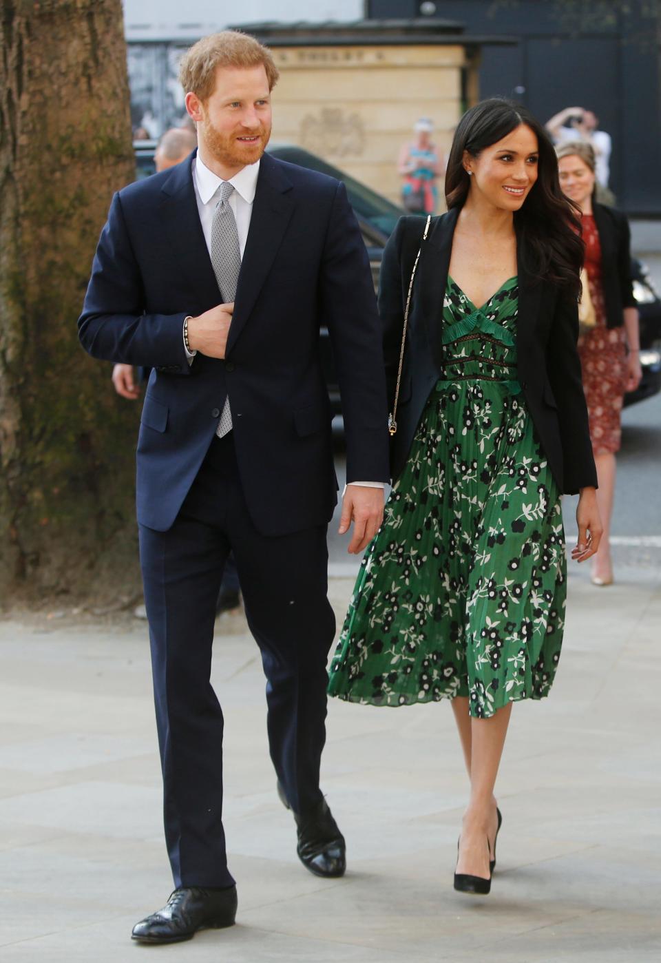 Harry in a dark navy suit and Meghan in a blazer with a green floral tea-length dress and heels.