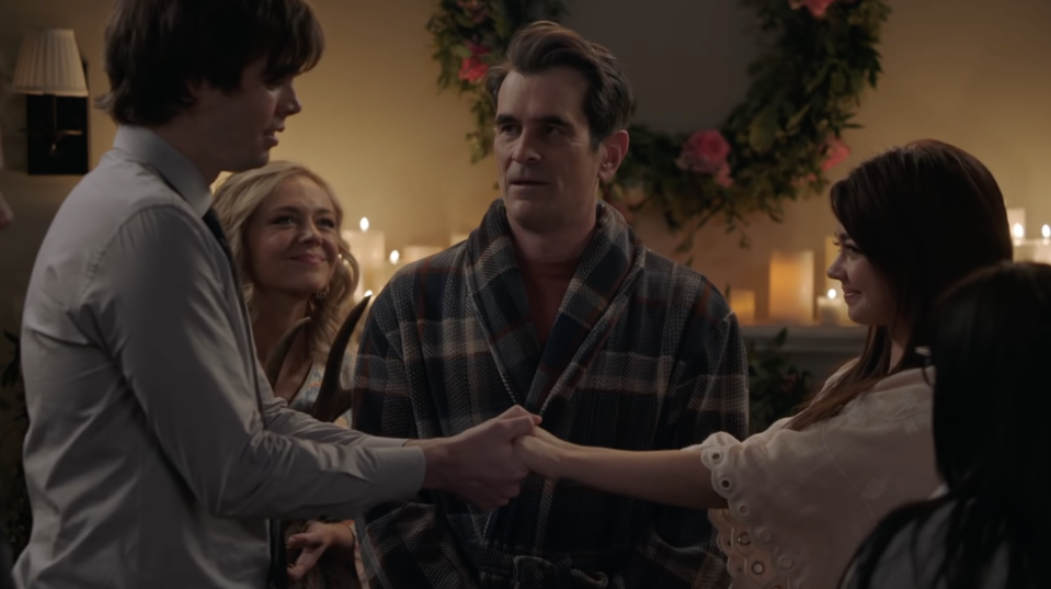 Phil stands in a bathrobe in front of the mantlepiece covered in candles, in front of him Dylan and Haley are standing an arm's width apart, facing each other and holding hands