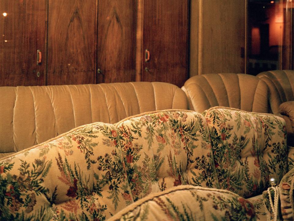 Floral-pattern and yellow couches in front of wooden paneling on blue wall and golden chandelier hanging down