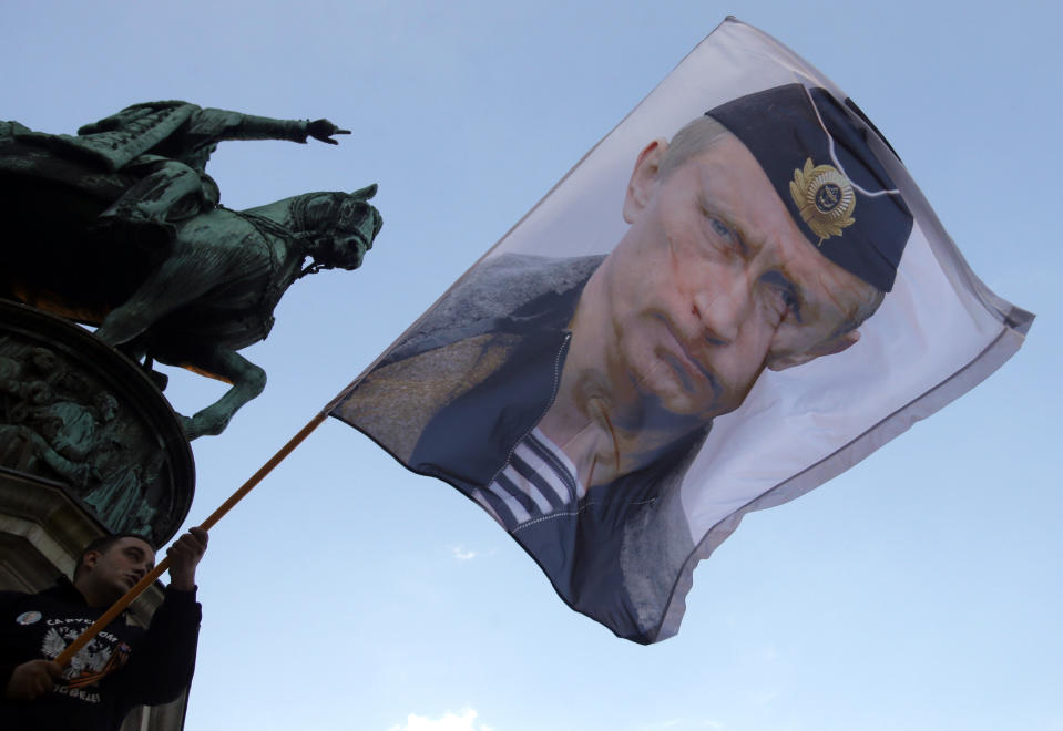 FILE - In this Saturday, Sept. 24, 2016, file photo, a man waves a flag showing Russian President Vladimir Putin, in front of the monument of late Serbian Duke Mihailo Obrenovic, during a meeting where show their support for a referendum in Republika Srpska, in Belgrade, Serbia. Vladimir Putin has accused the U.S. and the West of destabilizing the Balkans with NATO expansion policies as Serbia prepares a hero's welcome for the Russian president. (AP Photo/Darko Vojinovic, File)