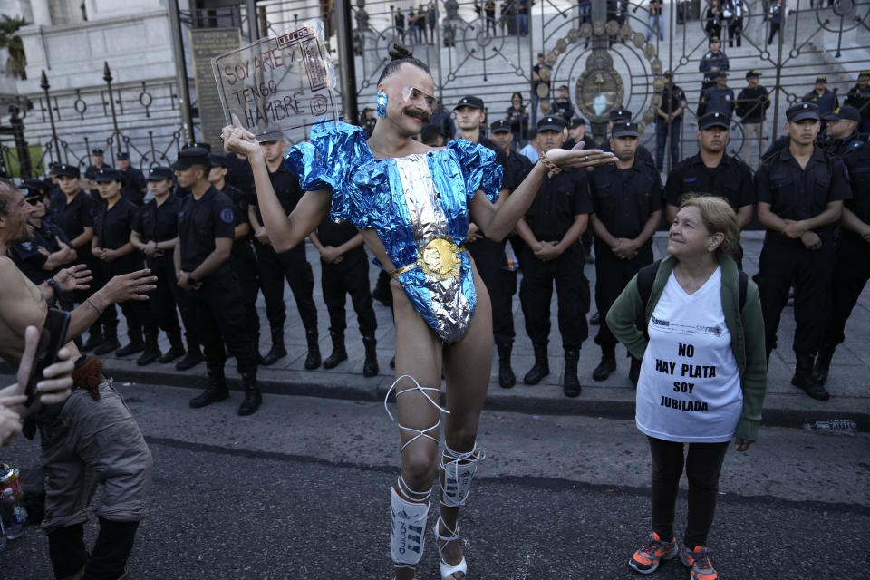 Vick Teker, dressed in a national flag outfit holding a sign with a message that reads in Spanish: "I am art and I am hungry", and a woman wearing a T-shirt with a message that reads: "There is no money. I am retired", take part in a demonstration outside Congress as part of a national strike to protest the economic and labor reforms proposed by Argentine President Javier Milei in Buenos Aires, Argentina, Jan. 24, 2024. (AP Photo/Rodrigo Abd)