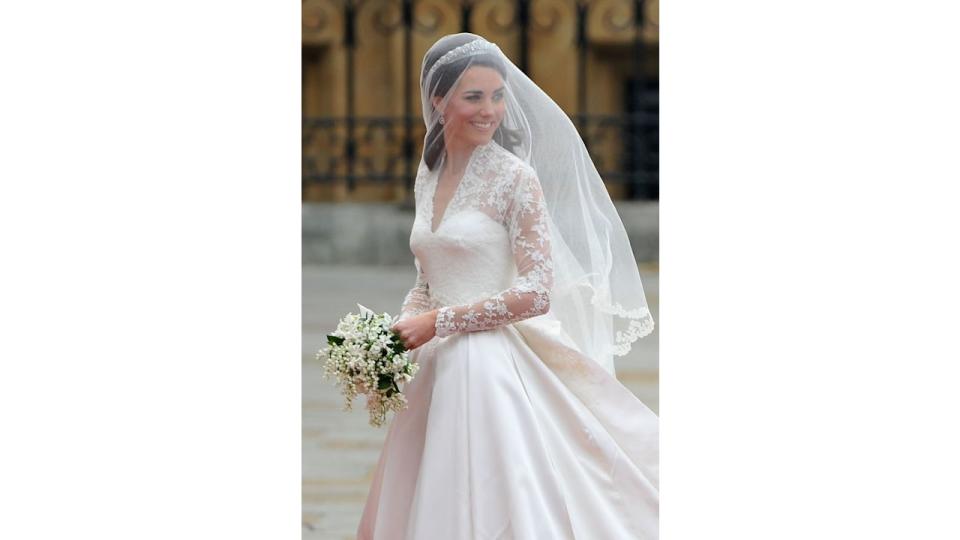 Kate Middleton wearing a veil and a wedding dress looking over her shoulders