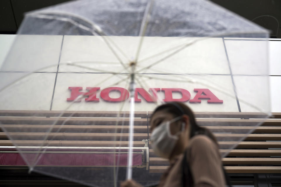 A woman walks in the rain near the logo of Honda Motor Company Friday, May 13, 2022, in Tokyo. Honda’s fiscal fourth quarter profit slipped to almost half of what the Japanese automaker earned the previous year amid headwinds of supply shortages and rising raw material costs. (AP Photo/Eugene Hoshiko)