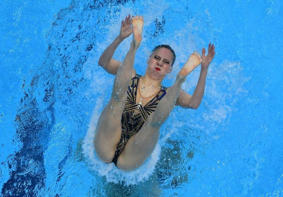 View of a swimmer descending into the water with legs slightly apart, arms raised, eyes closed, and appearing to hold their breath with great intensity