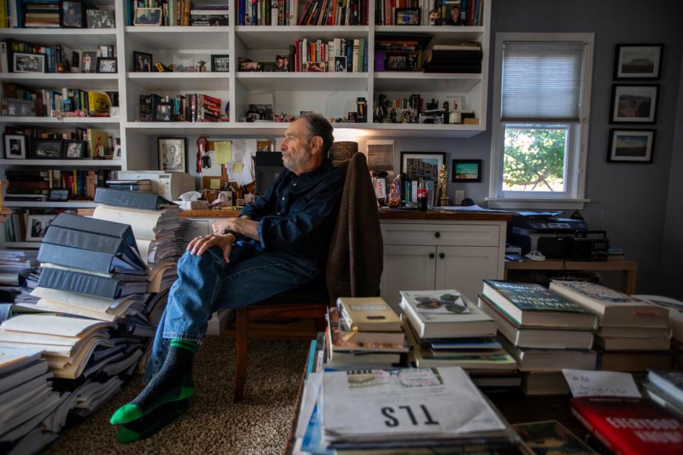 A man sits in a room before shelves filled with books.