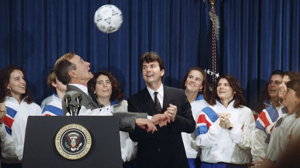 President George Bush heads a ball while meeting the 1991 Women's World Cup champions in 1992. Anson Dorrance looks on with his players. - Barry Thumma/AP