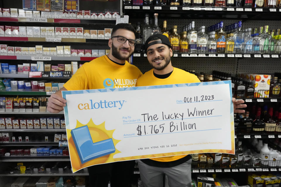 Jonathan Khalil, left, and Chris Khalil, sons of the store co-owners, hold up a ceremonial check presented to them by lottery officials at the Midway Market & Liquor store, Thursday, Oct. 12, 2023, in Frazier Park, Calif., where a $1.765 billion winning Powerball ticket was sold. (AP Photo/Marcio Jose Sanchez)