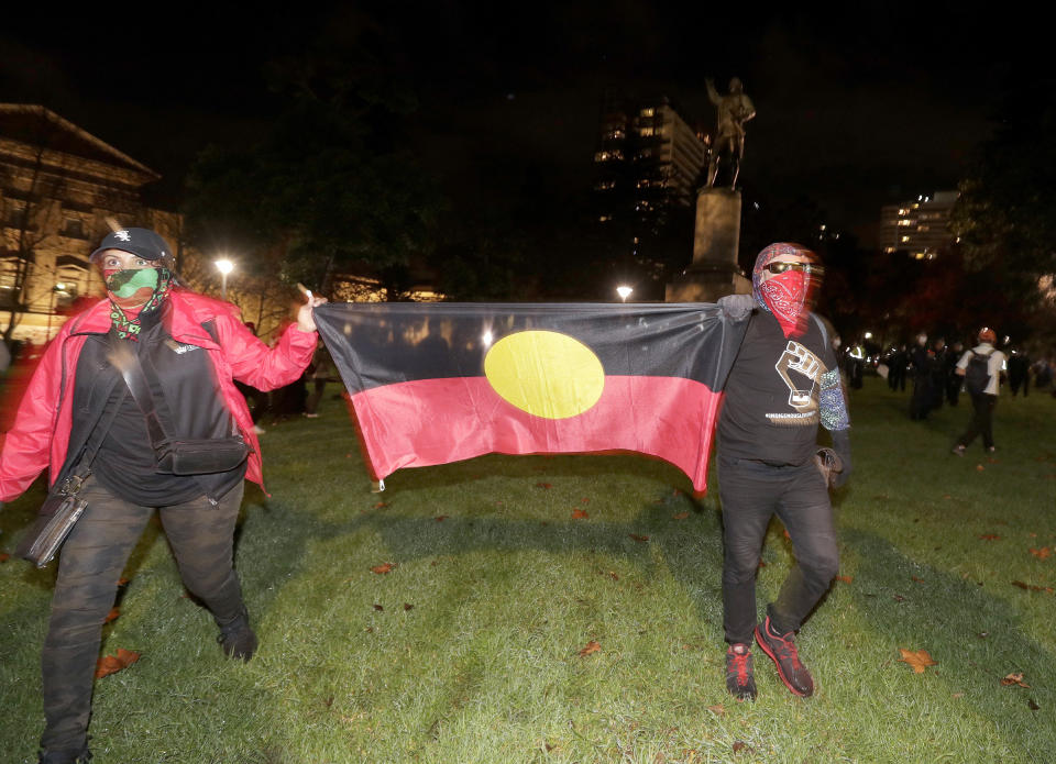 Protestoers carry an Aboriginal flag as the walk past a statue of British explorer James Cook in Sydney, Friday, June 12, 2020, to support U.S. protests over the death of George Floyd. Hundreds of police disrupted plans for a Black Lives Matter rally but protest organizers have vowed that other rallies will continue around Australia over the weekend despite warnings of the pandemic risk. (AP Photo/Rick Rycroft)