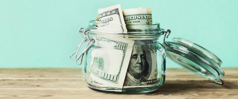 Dollar bills in glass jar on wooden table. Saving money concept.