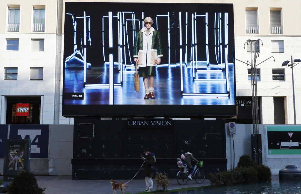 People stand at the bottom of a giant screen streaming a Fendi fashion live show during the Milan's fashion week in Milan, Italy, Friday, Jan. 15, 2021. (AP Photo/Antonio Calanni)