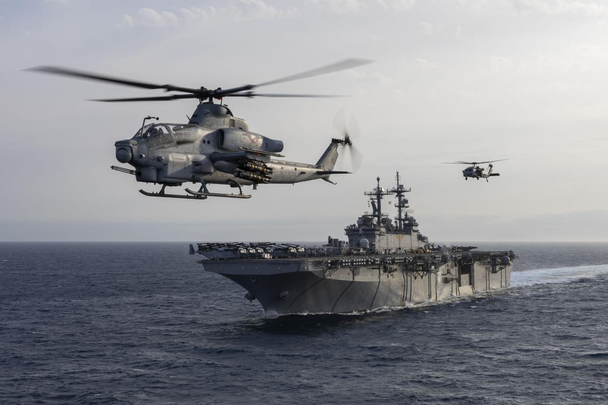 Two helicopters flying near an amphibious assault ship at sea.